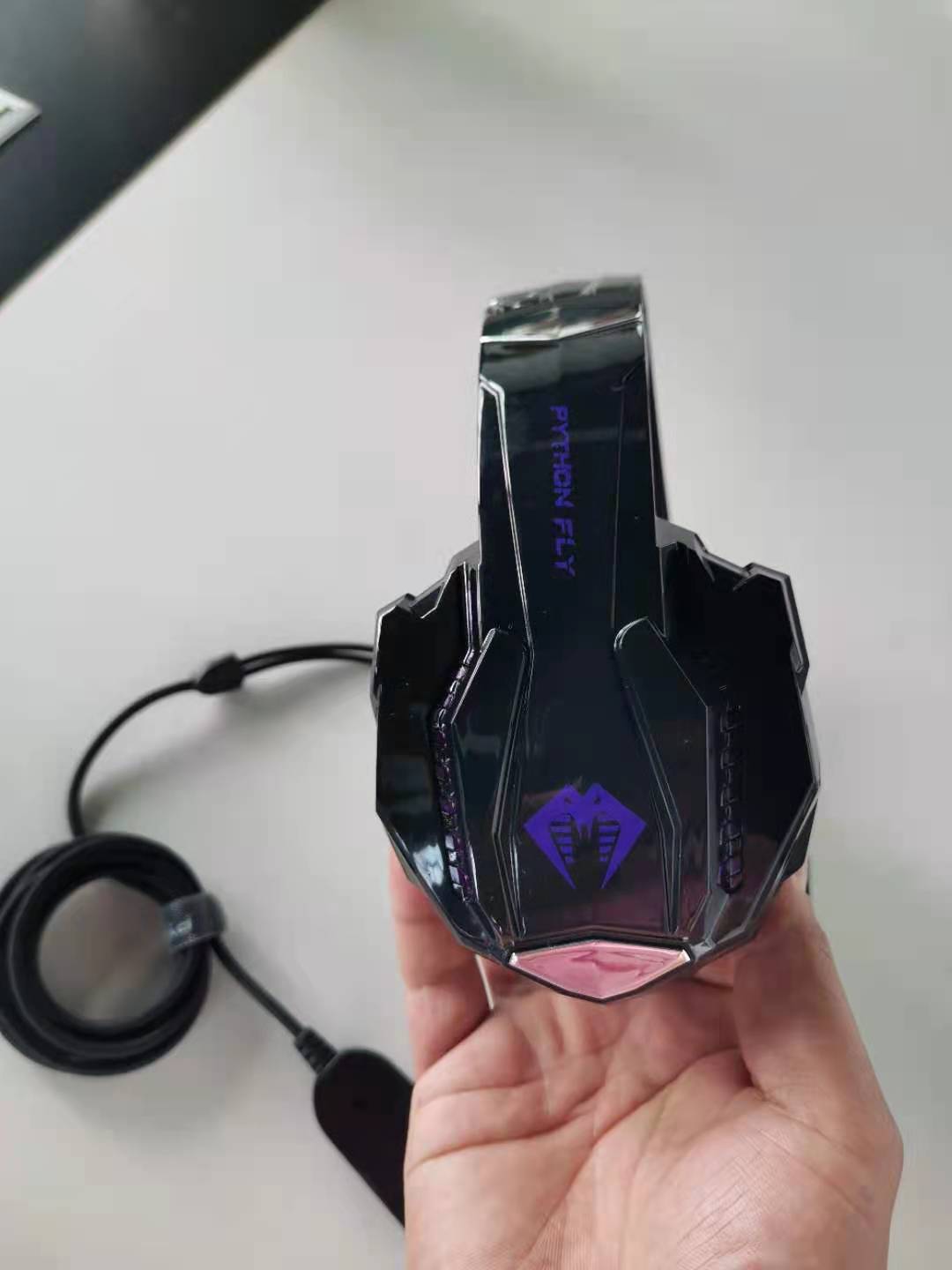 Gaming headset with cable held in a hand on a white surface