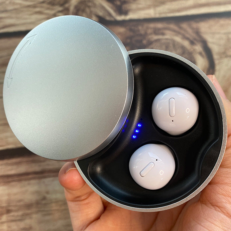 Wireless earbuds in a charging case held by a hand on a wooden surface