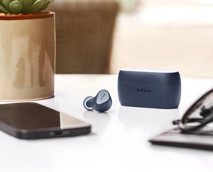 Jabra wireless earbuds and charging case on a desk with a smartphone and glasses.
