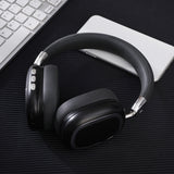 Black over-ear headphones on a dark surface with a keyboard and notebook in the background