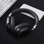 Black over-ear headphones on a dark surface with a keyboard and notebook in the background