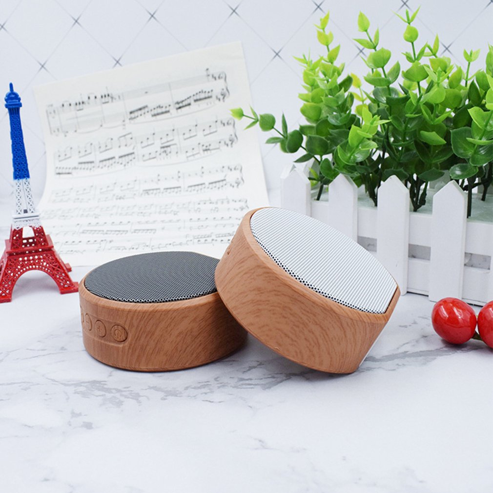 Wooden and gray speaker on a white surface with decorative items in the background
