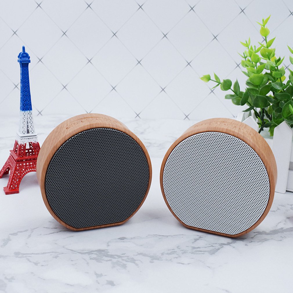 Two round speakers with wooden exteriors on a marble surface with decorative items in the background.