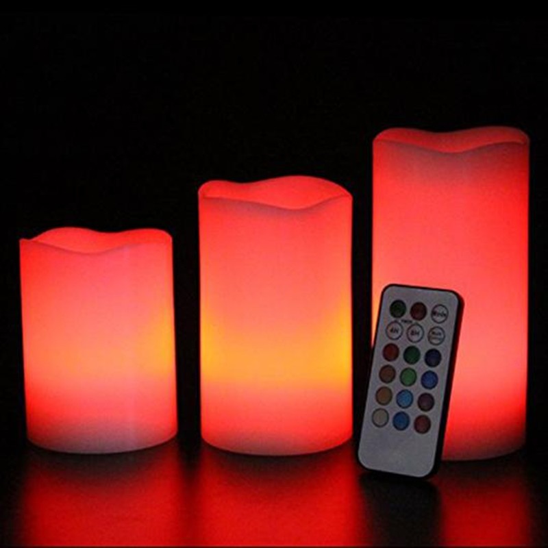 Set of three colorful LED candles with a remote control on a dark background