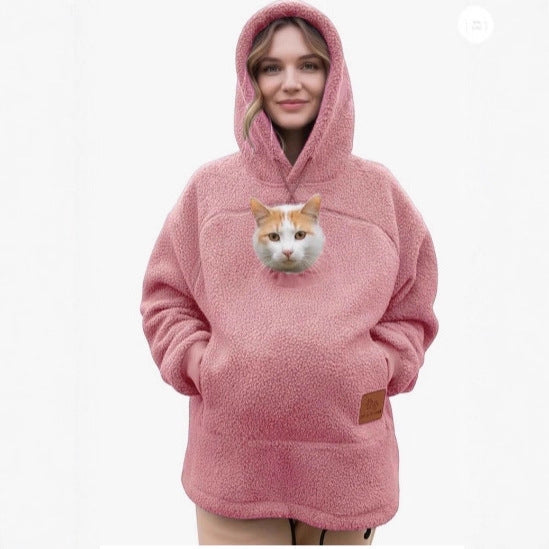 A woman wearing a pink sherpa fleece hoodie with a realistic cat face printed on the front chest, set against a plain white background.