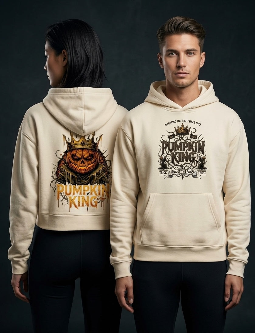 A man and a woman modeling matching cream-colored hoodies against a dark studio background. The woman shows the back graphic, which features a jack-o'-lantern wearing a crown and the words 'Pumpkin King'.